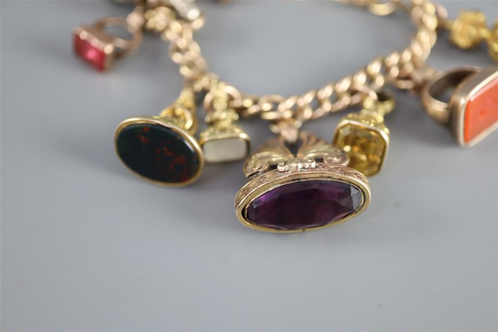 An early 20th century 9ct gold charm bracelet hung with thirteen assorted gold or gilt metal overlaid gem set fob seals,